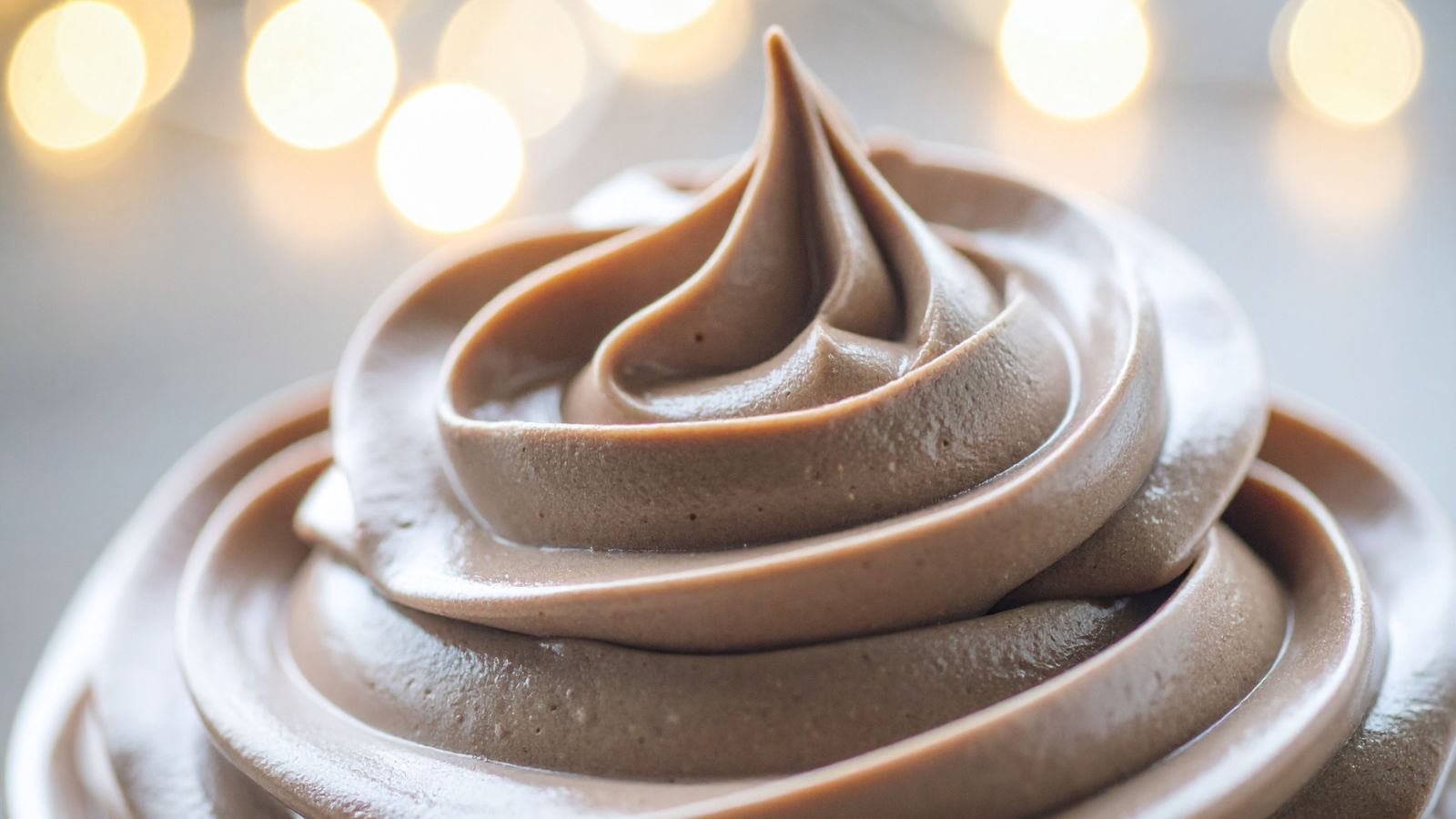 Creamy Chocolate Frosting Swirl with Festive Bokeh Lights Background.