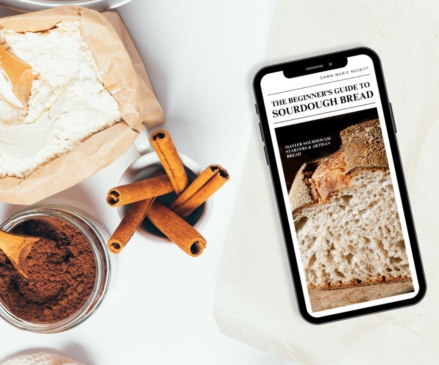 Sourdough baking guide ebook on a mobile device and on a baking flatlay surrounded by dark chocolate and cinnamon sticks for baking a brownie