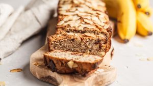 Home made banana bread with almonds and chocolate on a wooden platter with a grey background