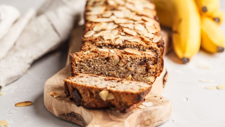 Home made banana bread with almonds and chocolate on a wooden platter with a grey background